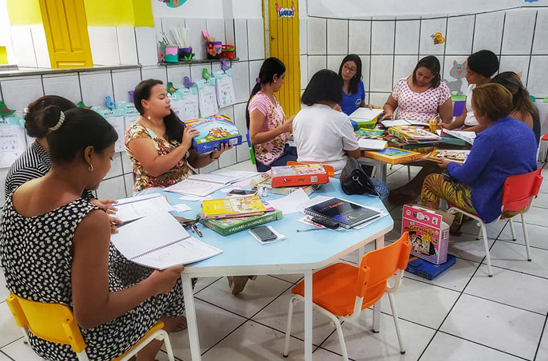 Crianças e responsáveis em torno das mesas durante atividade em sala