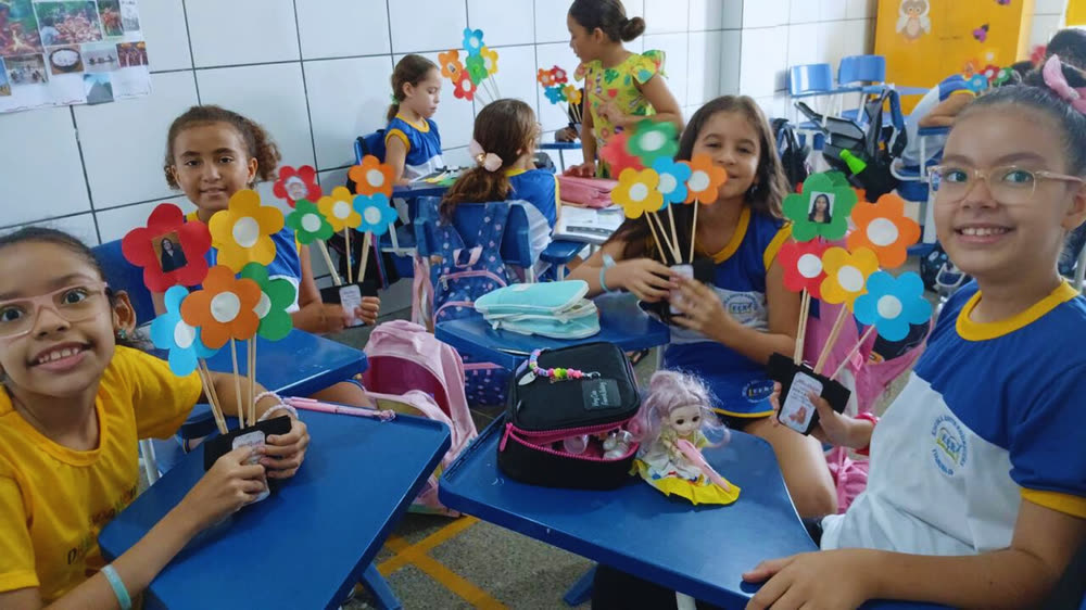Crianças da Educação Infantil em volta da mesa com flores de papel que produziram